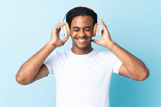 Νεαρός Αφροαμερικανός με κοτσίδες απομονωμένες σε μπλε φόντο ακούγοντας μουσική - Φωτογραφία, εικόνα