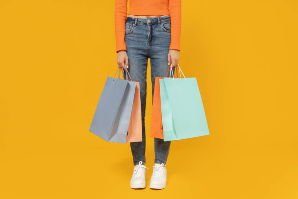 Junges Mädchen mit Einkaufstaschen auf gelbem Hintergrund. - Foto, Bild