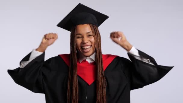 chica africana feliz en una túnica negra y un sombrero de maestros se regocija y baila sobre un fondo blanco - Metraje, vídeo