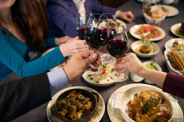 Menschen sitzen an einem festlichen Tisch in einem Restaurant und klimpern mit Weingläsern - Foto, Bild