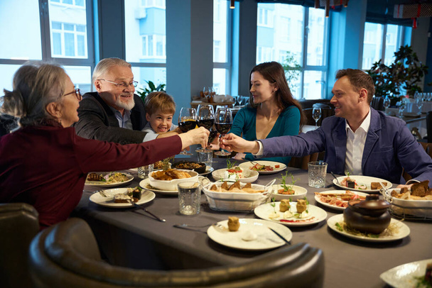 Happy family holding glasses with wine while celebrating Christmas in the restaurant - Photo, Image