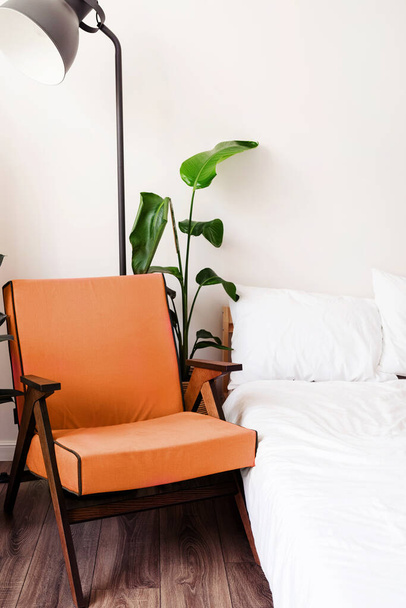 2024 yılının rengi: Şeftali tüyü. Beyaz duvarın yanında rahat mor sandalyeli, yataklı ve bitkili şık bir oda. - Fotoğraf, Görsel