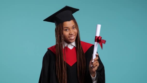 boldog afrikai lány fekete köntösben és mesterkalapban mutatja diploma, csók és ölelés. Kiváló minőségű 4k felvételek - Felvétel, videó