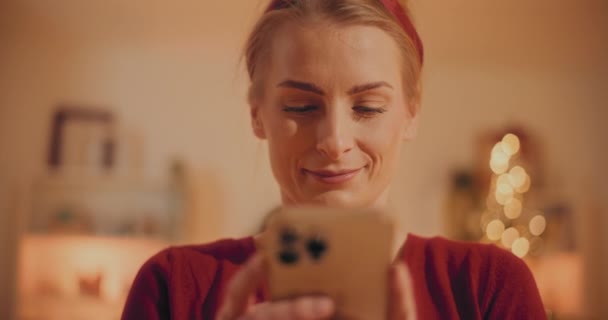 Relajado Mujer joven Navegación Smartphone Desplazamiento de medios sociales Compras en línea durante la Navidad - Metraje, vídeo