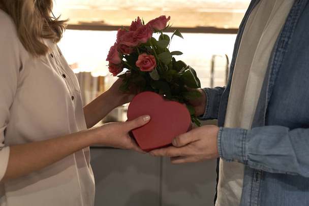 Ο άντρας δίνει ένα κουτί σοκολατάκια και τριαντάφυλλα στην αγαπημένη του γυναίκα.  - Φωτογραφία, εικόνα