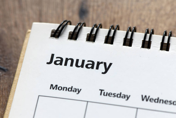 λέξη ΙΑΝΟΥΑΡΙΟΣ στο ημερολόγιο σε ένα ξύλινο τραπέζι. Η αρχή του έτους, ο πρώτος μήνας είναι ο χρόνος για να προετοιμαστεί για ολόκληρο το έτος. - Φωτογραφία, εικόνα