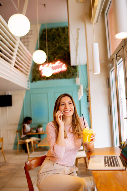 Jonge vrouw werkt op een laptop en drinkt vers sinaasappelsap in het café - Foto, afbeelding