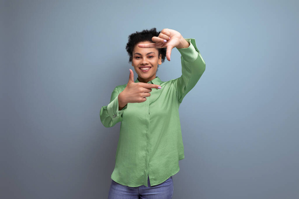 νεαρή θετική Λατίνα γυναίκα ντυμένη με ένα πράσινο πουκάμισο χαμογελώντας στο παρασκήνιο με αντίγραφο χώρο. - Φωτογραφία, εικόνα