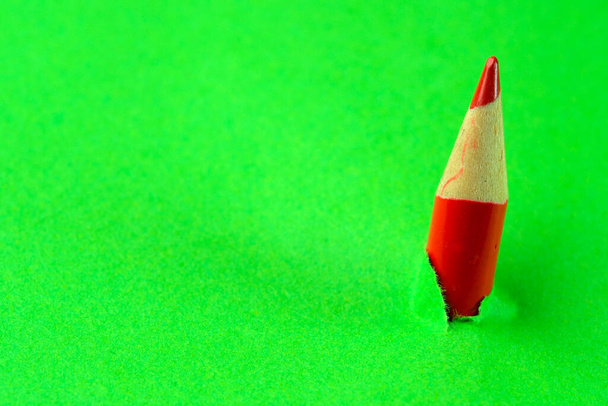 Small red pencil breaking through green stationery paper, abstract conceptual background, macro - Photo, Image