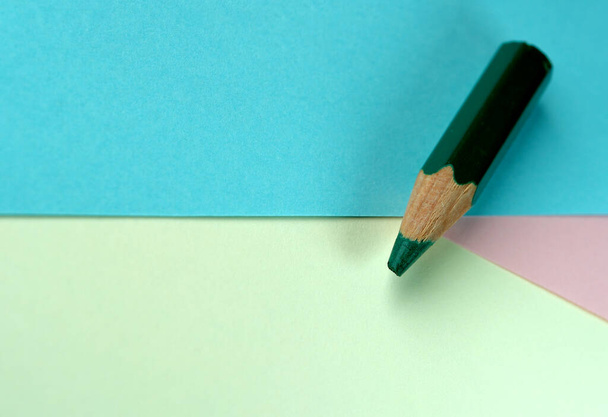 Un pequeño lápiz verde se encuentra en hojas de papel de colores, fondo de papelería, macro - Foto, imagen