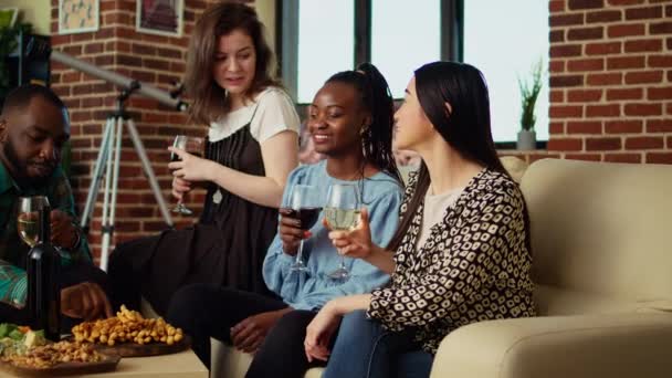 Multiethnic group of friends talking with each other in cozy apartment, gathered together to celebrate holiday. Multiethnic colleagues socializing at home during social event - Footage, Video