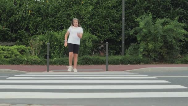 adolescente en auriculares salta alegremente la carretera a través de un cruce peatonal. Imágenes de alta calidad 4k - Imágenes, Vídeo