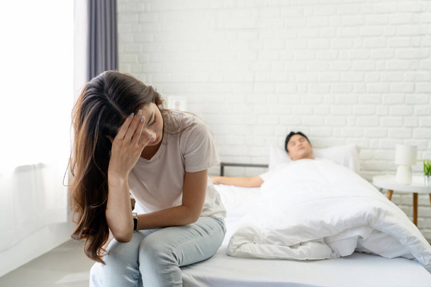 Stressaantunut aasialainen nainen istuu itkien sängyssä, kun hänen miehensä nukkuu. Käsitys perheongelmista ja avioliiton jälkeen. - Valokuva, kuva