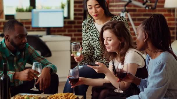 Diverse friends at apartment party using smartphone to laugh at social media posts made by acquaintance. Amused guests in living room gossiping about cringe images posted online by mate - Footage, Video