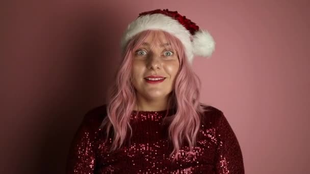 Έκπληκτη νεαρή γυναίκα φορώντας Χριστούγεννα Σάντα καπέλο στέκεται λαβή παλάμη, ανοιχτό στόμα ουρλιάζοντας ναι γιορτάζει τη νίκη απομονώνονται σε παστέλ ανοιχτό ροζ χρώμα φόντο. Υψηλής ποιότητας υλικό FullHD - Πλάνα, βίντεο