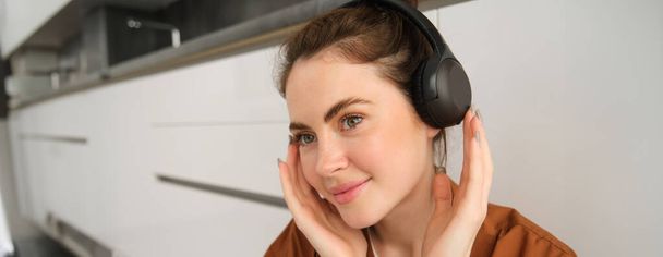 Εικόνα της σύγχρονης γυναίκας, όμορφο κορίτσι απολαμβάνει να ακούει μουσική, έχει μαύρο ασύρματα ακουστικά, κάθεται στο πάτωμα και ξεκουράζεται. - Φωτογραφία, εικόνα