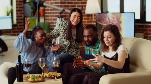 BIPOC-ystävät ottavat ryhmäkuvia selfie-kameran älypuhelimella asunnonjuhlissa. Iloiset kaverit modernissa kodissa poseeraavat valokuvan kanssa viiniä ja samppanjalaseja, tehdä eleitä - Materiaali, video