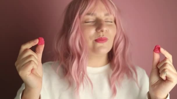 Jovem caucasiana positiva ou mulher comendo doces de geleia doce contra fundo rosa. Imagens FullHD de alta qualidade - Filmagem, Vídeo