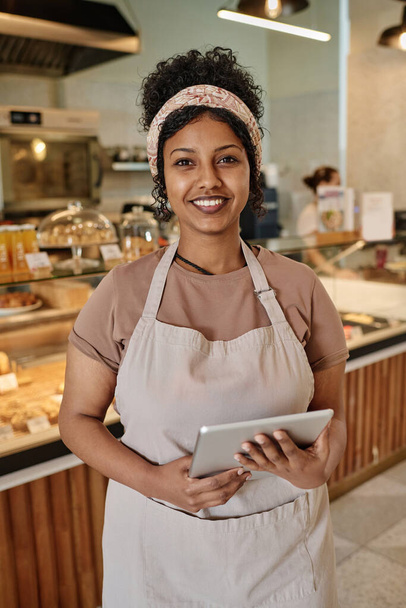 地元のパン屋のウェイトレスは,デジタルタブレットを保持し,カメラで微笑んでいる彼女の職場でポーズ - 写真・画像