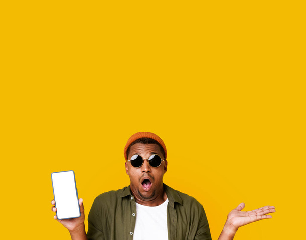 Exited African American Man In Trendy Glasses In Mobile App Advertisement Isolated Over Yellow Color Background. Young Smiling Cheerful Satisfied Positive Happy Black Man 20s In Casual Basic Closing - Фото, изображение
