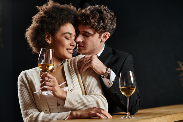 schöner Mann flirtet mit afrikanisch-amerikanischer Frau, die beim Date mit einem Weinglas am Tresen sitzt - Foto, Bild