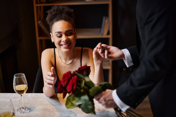 セントバレンタインデーのレストランで陽気なアフリカ系アメリカ人女性の手を握るスーツの男 - 写真・画像