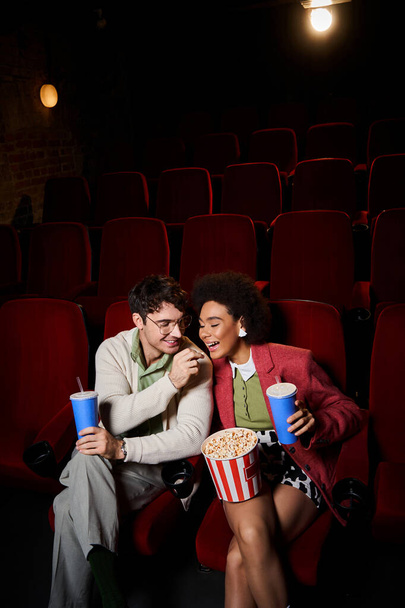 日付の映画館で彼のアフリカのアメリカのガールフレンドとポップコーンを共有するメガネのハンサム男 - 写真・画像