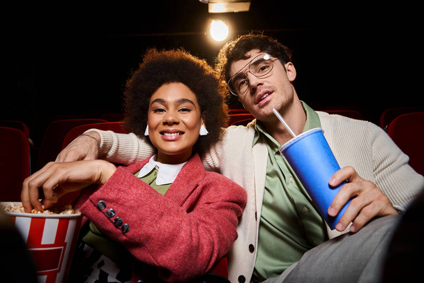 cheerful multiethnic couple in trendy clothes sharing popcorn and smiling at camera, Valentines day - Photo, Image
