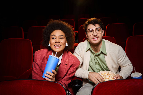 cheerful young diverse couple in trendy clothes watching movie and smiling at cinema, Valentines day - Photo, Image