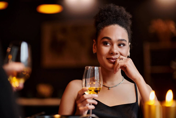 fröhliche afrikanisch-amerikanische Frau lächelnd und mit einem Glas Wein beim Date am Valentinstag - Foto, Bild