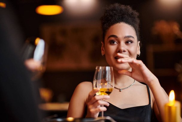 giovane donna afroamericana sorridente e con un bicchiere di vino in mano durante la data di San Valentino - Foto, immagini