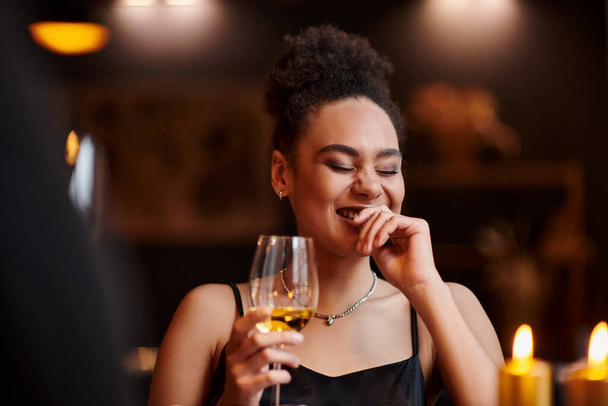curly african american woman laughing and holding glass of wine during date on Valentines day - Photo, Image