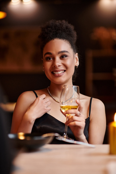 fröhliche afrikanisch-amerikanische Dame lächelnd und mit einem Glas Wein beim Date am Valentinstag - Foto, Bild