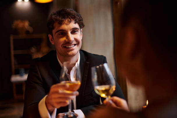ευτυχισμένος όμορφος άντρας χαμογελάει και κοιτάζει τη φίλη του κατά τη διάρκεια του ραντεβού του Αγίου Βαλεντίνου, ρομαντικό δείπνο - Φωτογραφία, εικόνα