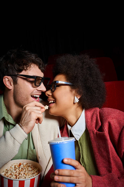 handsome man with glasses sharing popcorn with his beautiful jolly african american girlfriend - Photo, Image
