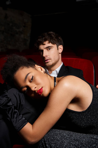 attraktive junge multiethnische Paar in schwarzen eleganten Outfits posiert im Kino, Valentinstag - Foto, Bild