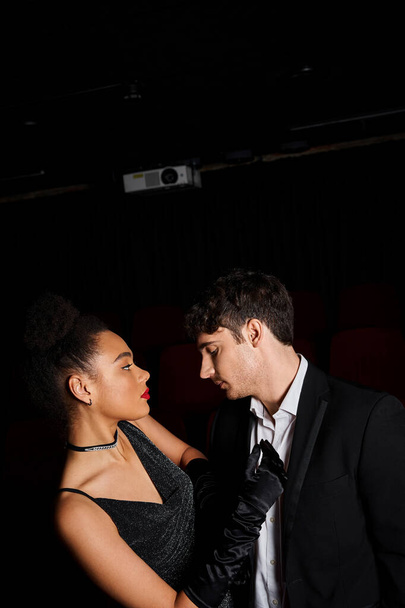 αισθησιακό νεαρό πολυπολιτισμικό ζευγάρι με μαύρες ενδυμασίες που κοιτάζονται στο σινεμά ραντεβού - Φωτογραφία, εικόνα