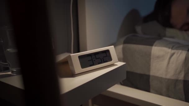 Sad man waking up lying awake on bed, closing eyes, yawning, suffering from insomnia sleep disorder with alarm clock. Man unable to sleep. Exhausted and tired. Alarm clock on nightstand and in bedroom - Footage, Video