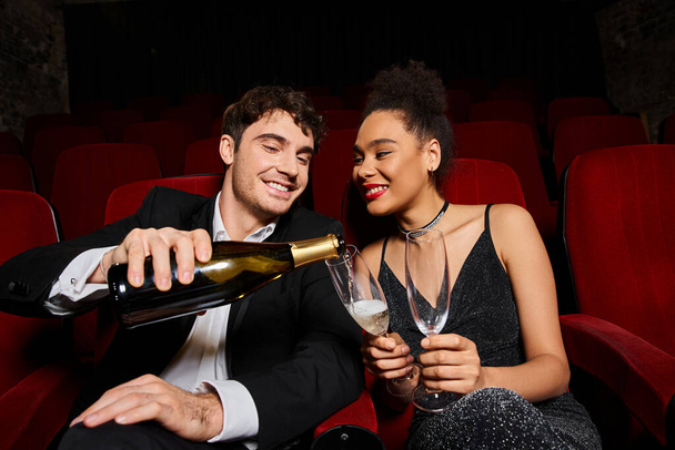 feliz pareja interracial disfrutando de una cita con champán en el cine y sonriendo felizmente, el día de San Valentín - Foto, imagen