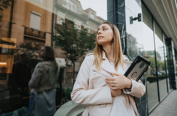 Femme d'affaires posant dans la ville, tenant une tablette, debout devant un bâtiment de mur de verre. - Photo, image