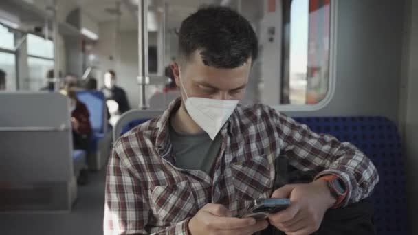 Ontspannen man met KN95 FFP2 masker op zijn gezicht met behulp van smartphone applicatie. Passagier gemaskeerd in spoorweg reizen terwijl gezeten op wagen en sms 'en op zijn mobiele telefoon. Veilig reizen met het openbaar vervoer.  - Video