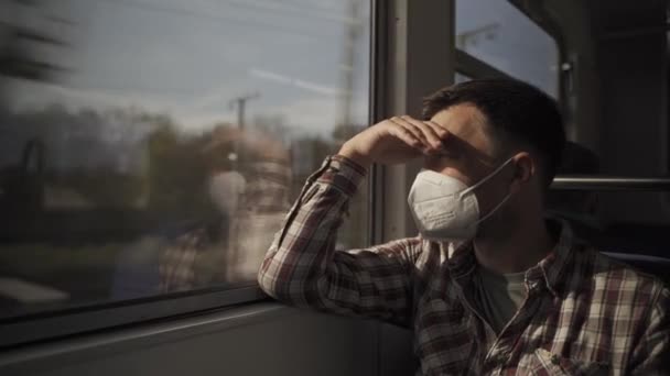 Unavený depresivní dojíždějící muž v ochranné masce proti koronavirové infekci sedí ve vlaku a dívá se z okna. New Normal. Společenská vzdálenost při cestování veřejnou dopravou.  - Záběry, video