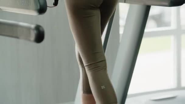 女の子アスリートがトレッドミルに乗る。 女性はトレーニング前に脚の筋肉を温める. スポーツ用具を使用した軽い身体活動. クローズアップ。 高品質の4k映像 - 映像、動画