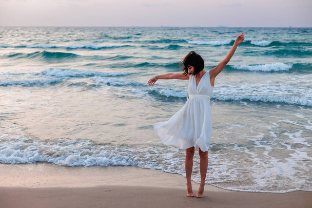 Щаслива дівчина-мандрівник у білій літній сукні насолоджується пляжем тропічного раю з бірюзовим морем. Щаслива молода жінка в красивій білій сукні ходить уздовж пляжу під час заходу сонця.  - Фото, зображення
