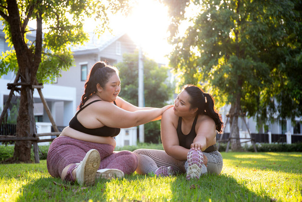 Ожиріння двох молодих азіатських жінок, які роблять розтягнуту ногу в парку, жінка з надмірною вагою розігрівається і займається дієтою і здоров'ям, тренуванням і мотивацією, надмірною і викликом, плюс розмір. - Фото, зображення
