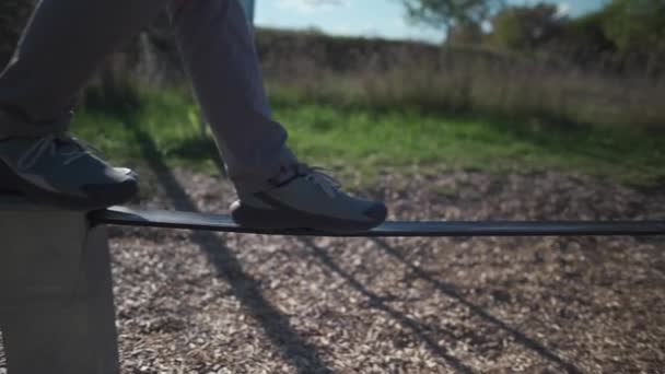 Homem iniciante em sapatos aprende a andar e manter o equilíbrio na borracha slackline no parque na Alemanha. Homem equilibra em corda esticada no ginásio da cidade em Munique. Desleixado. Banda fraca. Balanceamento corda de borracha.  - Filmagem, Vídeo