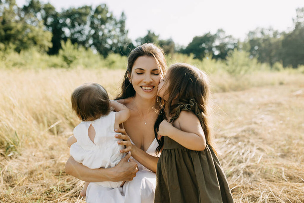 Mutter verbringt Zeit mit Kindern an einem Sommertag im Freien. Kleines Mädchen küsst ihre Mutter auf die Wange. - Foto, Bild