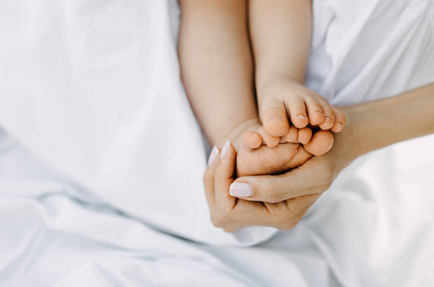 Detailní záběr na maminky ruku drží dítě bosé nohy. - Fotografie, Obrázek