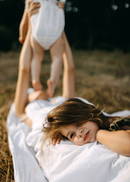 Κοριτσάκι ξαπλωμένο στις μανάδες ενώ η μητέρα παίζει με το άλλο παιδί..  - Φωτογραφία, εικόνα