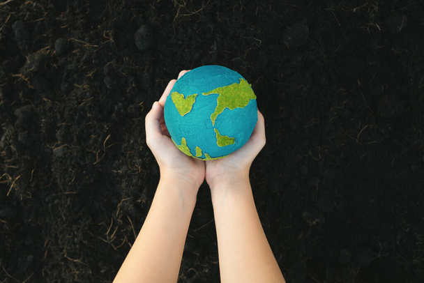 Jovens meninos mão segurando planeta Terra globo no fundo do solo fértil como dia da Terra para salvar este planeta com o princípio ESG e energia amiga do meio ambiente para um futuro mais brilhante. Giro - Foto, Imagem